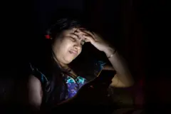 ਪਰੇਸ਼ਾਨ ਮਹਿਲਾ, ਹਨੇਰੇ ਵਿੱਚ ਬੈਠੀ ਹੈ ਅਤੇ ਮੂੰਹ ਉੱਤੇ ਮੋਬਾਈਲ ਸਕੀਰਨ ਦੀ ਰੌਸ਼ਨੀ ਪੈ ਰਹੀ ਹੈ, ਬਾਕੀ ਕਮਰੇ ਵਿੱਚ ਹਨੇਰਾ ਹੈ