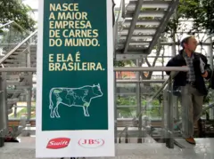Pôster com a legenda escrita em amarelo sobre um fundo verde escuro, com um desenho de uma vaca que tem o mapa-múndi pintado sobre ela e os logotipos da Swift e da JBS abaixo.