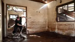 Mulher usa rodo para tentar limpar casa cheia de lama