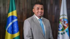 TH Joias em retrato formal na Alerj, com bandeiras do Brasil e do RJ atrás