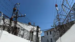 Paredes brancas cobertas de arame farpado, em dia de céu azul