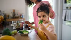 طفلة تقف في المطبخ أمام طاولة تشتم البروكلي