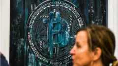 A woman walks past a Bitcoin themed art installation during the Bitcoin 2022 Conference at the Miami Beach Convention Center in Miami Beach, Florida, on April 7, 2022.