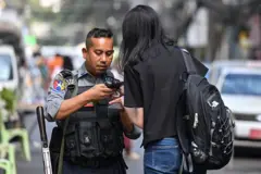 ရန်ကုန်မြို့မှာ ပြီးခဲ့တဲ့ ဒီဇင်ဘာလ ၂၈ ရက်တုန်းက မဲရုံထဲ ဝင်မယ့် အမျိုးသမီးတစ်ဦးကို စစ်ဆေးနေတဲ့ ရဲတပ်ဖွဲ့ဝင်တစ်ဦး 