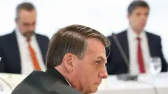 Bolsonaro de perfil, em reunião, com dois de seus ministros ao fundo