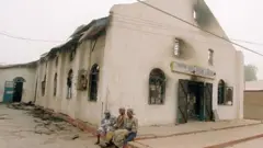 Three women siddon for di front of one burnt church 