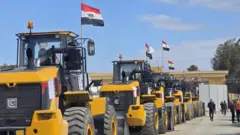 Imagens de vários caminhões grandes transportando contêineres e equipamentos pesados de construção enviados do Egito para Gaza, alinhados esperando no lado egípcio da passagem de fronteira de Rafah para entrar em Gaza