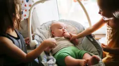 Две девочки общаются с младенцем в переноске