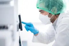 Un médico con guantes, gorro y una máscara frente a un dispositivo