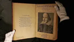 A primeira edição original de uma obra de Shakespeare, aberta entre as mãos cobertas por luvas de um funcionário de uma casa de leilões