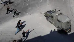 فلسطينيون يلقون بالحجارة على مركبة عسكرية إسرائيلية خلال مداهمة بالقرب من للجيش الإسرائيلي في الضفة الغربية التي تحتلها إسرائيل، 1 سبتمبر/أيلول، 2023.
