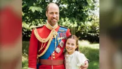 Prince William is wearing the scarlet dress uniform of the Welsh Guards, of which he is colonel, and has his arm around Charlotte, who is wearing a cream dress.
