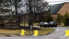 樹木の奥に建物があり、そこに続く道路に2台の車両がすれ違いの位置関係で見える。手前にはTEMPLE ISRAELの表示がある