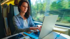 Biznesmenka siedzi przy stoliku w pociągu, pracując na laptopie podczas podróży