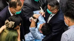 A pro-democrat lawmaker is restrained by security guards at the Legislative Council in Hong Kong during a row about a Chinese national anthem bill