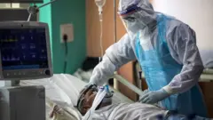 A medical staff member wearing Personal Protective Equipment (PPE) suit looks after a Covid-19 patient at the Intensive Care Unit of the Sharda Hospital, in Greater Noida near Delhi