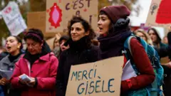 Mulheres em frente ao tribunal de Avignon, segurando cartazes em apoio a Gisèle Pelicot. Uma delas, na frente da imagem, segura uma placa de papelão escrita à mão com os dizeres em francês: "Obrigada, Gisèle".