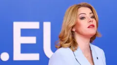 светловолосая женщина на фоне синего задника с буквами EU