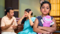 ਲੜਾਈ ਕਰਦੇ ਪਤੀ-ਪਤਨੀ ਅਤੇ ਉਦਾਸ ਖੜ੍ਹੀ ਬੱਚੀ ਦੀ ਸੰਕੇਤਕ ਤਸਵੀਰ 