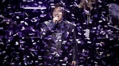 Javier Milei falando em um microfone durante evento. Há vários confetes caindo sobre ele