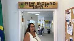 Lídia Souza usa camisa branca e está na soleira da porta do centro comunitário onde ela atua. Do lado esquerdo da imagem há uma bandeira brasileira.