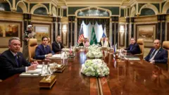 Steve Witkoff, Marco Rubio, Mike Waltz, o príncipe Faisal bin Farhan al-Saud, Mosaad bin Mohammad al-Aiban, Yuri Ushakov e Sergei Lavrov em mesa de reunião