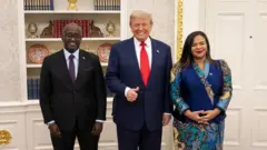 Minisitiri Olivier Nduhungirehe w'u Rwanda ibumoso yambaye isuti y'umukara amwenyura, Perezida Donald Trump hagati yambaye isuti y'ubururu bwijimye na karuvati y'umutuku yazamuye urutoki rw'igikumwe kandi aseka, na Minisitiri Therese Kayikwamba wa RD Congo yambaye imyembaro y'igitenge y'amabara arimo ubururu kandi amwenyura