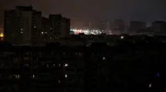 Блекаут у спальному районі Києва: лише в поодиноких вікнах багатоповерхівок видно світло. За ними – яскраво освітлена ліхтарями вулиця.