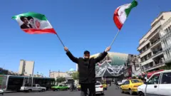 muškarac maše iranskim zastavama na trgu u teheranu