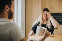 Homem usando laptop e mulher com dor de cabeça sentada à mesa 