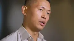 Jie Lijianは、閉じたスペースでBBCと話し、非の打ちどころのない白いシャツを着て、剃毛した剃毛された頭を持っています。