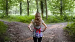 Mulher em uma mata olhando para duas estradas diferentes