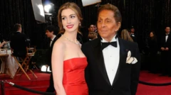 Oyuncu Anne Hathaway kırmızı bir elbiseyle ve yanında smokin içinde Valentino var.