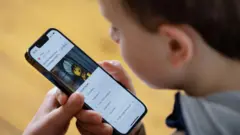 Мальчик, снятый сзади и немного сбоку, разглядывает экран смартфона