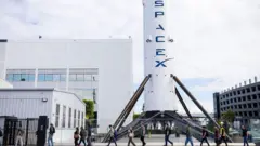 Uma fila de pessoas passa por um grande foguete branco com o logotipo azul Space X escrito nele.