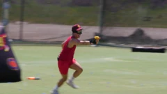 Ash está usando uma roupa vermelha em um campo e segura uma pistola de água
