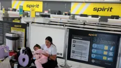 Una mujer colombiana con su hija de brazos, sentada en el counter vacío de Spirit Airlines