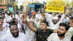 এসআইআর বিরোধী বিক্ষোভে পশ্চিমবঙ্গের মানুষ রাস্তায় প্রতিবাদ কর্মসূচি পালন করছেন। একজন বিক্ষোভকারীর হাতে ব্যানারে লেখা, “ভারতের নাগরিকদের বেনাগরিক করা চলবে না।”