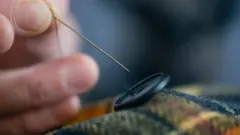 Mão costurando um botão em uma roupa