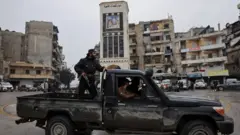 Bir pikap ara&ccedil; &uuml;zerinde ayakta duran silahlı bir Suriye ordu mensubu ve arkada Eşrefiye mahallesi