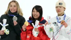 3人が横並びに立ち、片手でメダル、もう片手で大会マスコットのぬいぐるみを持っている。笑顔を見せている