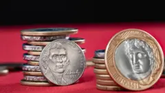 Duas pilhas, uma com moedas de dólar e outra de real, sobre superfície vermelha