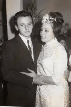 Alejandra Jáidar, con un elegante vestido blanco y un adorno blanco en el cabello, abraza a su hermano, quien está vestido de traje y corbata negros y una camisa blanca