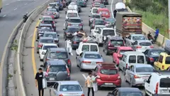 Carros parados em congestionamento em uma estrada, com pessoas vendendo produtos para os motoristas