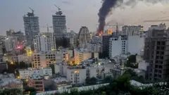 Sobre el cielo nocturno de Teherán se eleva humo procedente de los escombros del edificio de los medios de comunicación estatales iraníes tras un ataque aéreo israelí.