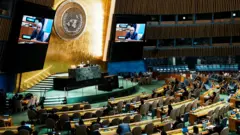رياض منصور، المراقب الدائم لفلسطين لدى الأمم المتحدة، على الشاشات أثناء مخاطبته المندوبين بعد تصويت الجمعية العامة للأمم المتحدة على قضية فلسطين وتنفيذ حل الدولتين، في مقر الأمم المتحدة في مدينة نيويورك، الولايات المتحدة، 12 سبتمبر/أيلول 2025.