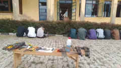 Awọn afurasi ajagungbalẹ ati afurasi adigunjale naa kọyin si kamẹra, awọn nnkan tawọn ọlọpaa gba lọwọ wọn wa lori bẹẹnṣi kan ti wọn to wọn si ninu aworan yii.