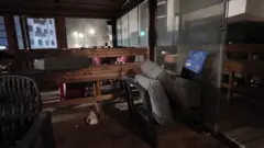 El interior oscuro de un bar muestra mesas y asientos tirados.