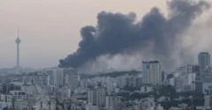 Imagem mostrando paisagem de prédios de Teerã e uma fumaça negra saindo de um dos prédios atingidos por bombardeios israelenses