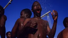 De jeunes hommes se douchent après avoir nagé le 1er janvier 2003 à Camps Bay, en Afrique du Sud.